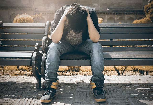 man in black shirt and gray denim pants sitting on gray padded bench